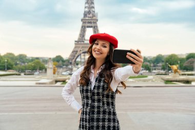 Beautiful young woman visiting paris and the eiffel tower. Parisian girl with red hat and fashionable clothes having fun in the city center and landmarks area