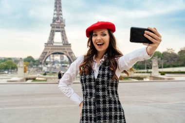Beautiful young woman visiting paris and the eiffel tower. Parisian girl with red hat and fashionable clothes having fun in the city center and landmarks area