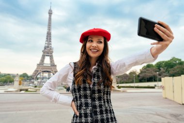Beautiful young woman visiting paris and the eiffel tower. Parisian girl with red hat and fashionable clothes having fun in the city center and landmarks area
