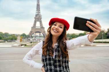 Beautiful young woman visiting paris and the eiffel tower. Parisian girl with red hat and fashionable clothes having fun in the city center and landmarks area