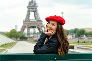 Beautiful young woman visiting paris and the eiffel tower. Parisian girl with red hat and fashionable clothes having fun in the city center and landmarks area