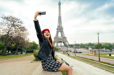 Beautiful young woman visiting paris and the eiffel tower. Parisian girl with red hat and fashionable clothes having fun in the city center and landmarks area