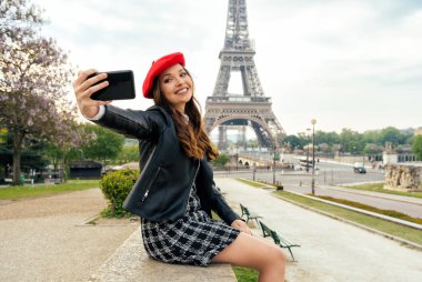 Beautiful young woman visiting paris and the eiffel tower. Parisian girl with red hat and fashionable clothes having fun in the city center and landmarks area