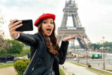 Beautiful young woman visiting paris and the eiffel tower. Parisian girl with red hat and fashionable clothes having fun in the city center and landmarks area