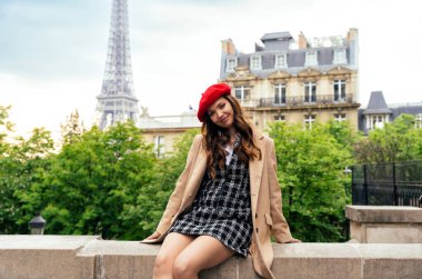 Beautiful young woman visiting paris and the eiffel tower. Parisian girl with red hat and fashionable clothes having fun in the city center and landmarks area