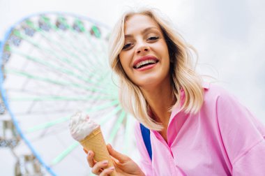 Beautiful young blond woman eating ice cream at amusement park - Cheerful caucasian female portrait during summertime vacation- Leisure, people and lifestyle concepts