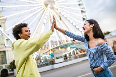 Multiracial young couple of lovers dating at theferry wheel in the amusement park - People with mixed races having fun outdoors in the city- Friendship, releationship and lifestyle concepts