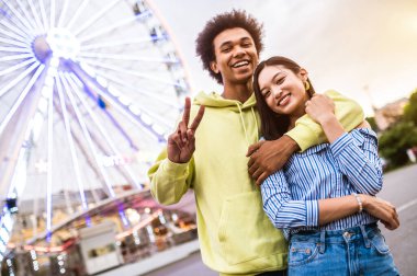 Multiracial young couple of lovers dating at theferry wheel in the amusement park - People with mixed races having fun outdoors in the city- Friendship, releationship and lifestyle concepts
