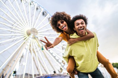Multiracial young couple of lovers dating at theferry wheel in the amusement park - People with mixed races having fun outdoors in the city- Friendship, releationship and lifestyle concepts