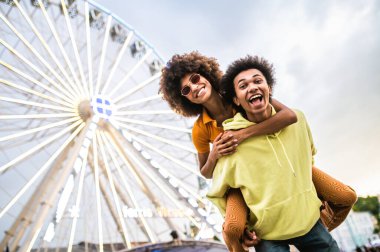 Multiracial young couple of lovers dating at theferry wheel in the amusement park - People with mixed races having fun outdoors in the city- Friendship, releationship and lifestyle concepts