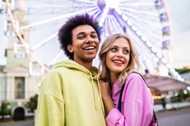 Multiracial young couple of lovers dating at theferry wheel in the amusement park - People with mixed races having fun outdoors in the city- Friendship, releationship and lifestyle concepts