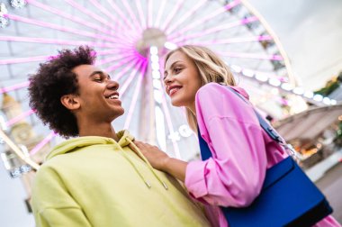 Multiracial young couple of lovers dating at theferry wheel in the amusement park - People with mixed races having fun outdoors in the city- Friendship, releationship and lifestyle concepts