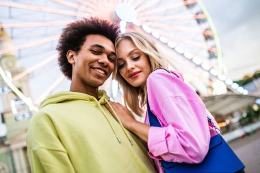 Multiracial young couple of lovers dating at theferry wheel in the amusement park - People with mixed races having fun outdoors in the city- Friendship, releationship and lifestyle concepts