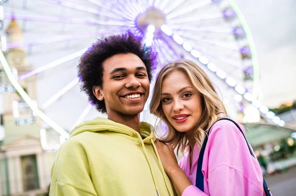 Multiracial young couple of lovers dating at theferry wheel in the amusement park - People with mixed races having fun outdoors in the city- Friendship, releationship and lifestyle concepts