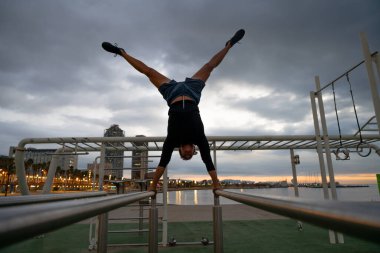 Sportive and athletic man doing functional training exercise at the outdoor gym - Adult athlete doing workout at sunrise at calisthenics park on the beach - Fitness, healthy lifestyle and sport concepts