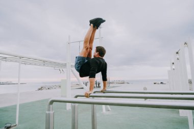 Sportive and athletic man doing functional training exercise at the outdoor gym - Adult athlete doing workout at sunrise at calisthenics park on the beach - Fitness, healthy lifestyle and sport concepts