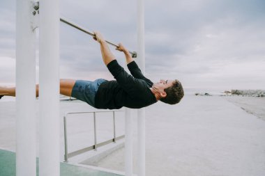 Sportive and athletic man doing functional training exercise at the outdoor gym - Adult athlete doing workout at sunrise at calisthenics park on the beach - Fitness, healthy lifestyle and sport concepts