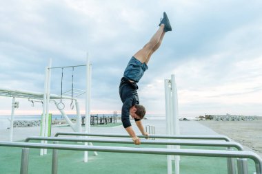 Sportive and athletic man doing functional training exercise at the outdoor gym - Adult athlete doing workout at sunrise at calisthenics park on the beach - Fitness, healthy lifestyle and sport concepts