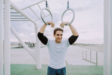 Sportive and athletic man doing functional training exercise at the outdoor gym - Adult athlete doing workout at sunrise at calisthenics park on the beach - Fitness, healthy lifestyle and sport concepts