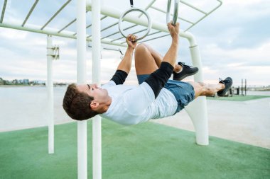 Sportive and athletic man doing functional training exercise at the outdoor gym - Adult athlete doing workout at sunrise at calisthenics park on the beach - Fitness, healthy lifestyle and sport concepts
