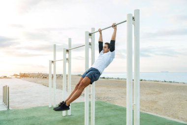 Sportive and athletic man doing functional training exercise at the outdoor gym - Adult athlete doing workout at sunrise at calisthenics park on the beach - Fitness, healthy lifestyle and sport concepts