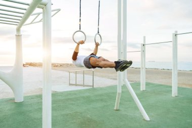 Sportive and athletic man doing functional training exercise at the outdoor gym - Adult athlete doing workout at sunrise at calisthenics park on the beach - Fitness, healthy lifestyle and sport concepts