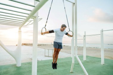 Sportive and athletic man doing functional training exercise at the outdoor gym - Adult athlete doing workout at sunrise at calisthenics park on the beach - Fitness, healthy lifestyle and sport concepts