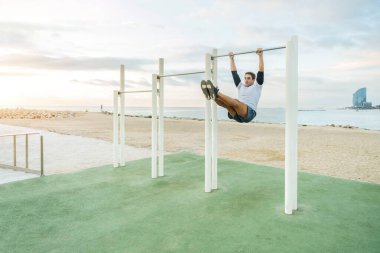 Sportive and athletic man doing functional training exercise at the outdoor gym - Adult athlete doing workout at sunrise at calisthenics park on the beach - Fitness, healthy lifestyle and sport concepts