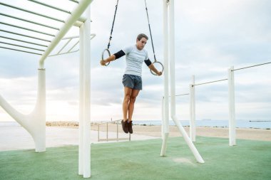 Sportive and athletic man doing functional training exercise at the outdoor gym - Adult athlete doing workout at sunrise at calisthenics park on the beach - Fitness, healthy lifestyle and sport concepts