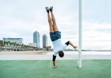 Sportive and athletic man doing functional training exercise at the outdoor gym - Adult athlete doing workout at sunrise at calisthenics park on the beach - Fitness, healthy lifestyle and sport concepts