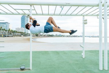Sportive and athletic man doing functional training exercise at the outdoor gym - Adult athlete doing workout at sunrise at calisthenics park on the beach - Fitness, healthy lifestyle and sport concepts
