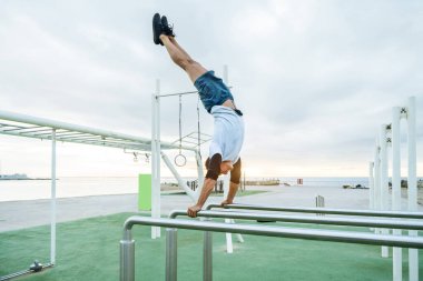 Sportive and athletic man doing functional training exercise at the outdoor gym - Adult athlete doing workout at sunrise at calisthenics park on the beach - Fitness, healthy lifestyle and sport concepts