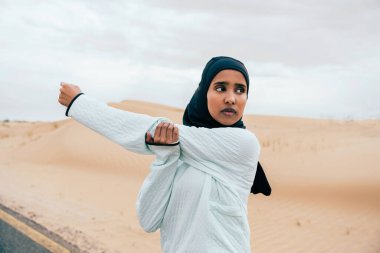 Ortadoğulu güzel bir Arap kadın çölde tesettür eğitimi alıyor sportif atletik müslüman kadın, burkini spor kıyafetleri giyiyor spor yapıyor.