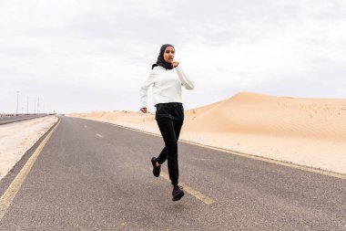 Ortadoğulu güzel bir Arap kadın çölde tesettür eğitimi alıyor sportif atletik müslüman kadın, burkini spor kıyafetleri giyiyor spor yapıyor.