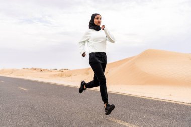 Ortadoğulu güzel bir Arap kadın çölde tesettür eğitimi alıyor sportif atletik müslüman kadın, burkini spor kıyafetleri giyiyor spor yapıyor.