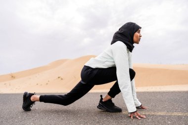 Ortadoğulu güzel bir Arap kadın çölde tesettür eğitimi alıyor sportif atletik müslüman kadın, burkini spor kıyafetleri giyiyor spor yapıyor.