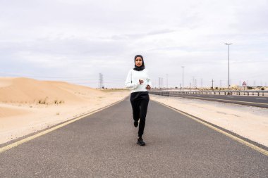 Ortadoğulu güzel bir Arap kadın çölde tesettür eğitimi alıyor sportif atletik müslüman kadın, burkini spor kıyafetleri giyiyor spor yapıyor.