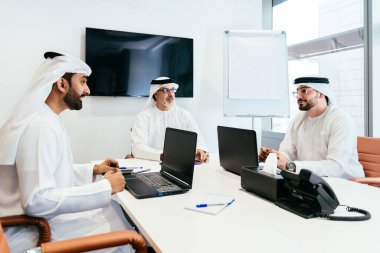 Dubai 'deki ofiste geleneksel emirati kıyafetleri giyen bir grup orta doğulu iş adamı BAE' de çalışıyor ve beyin fırtınası yapıyor.