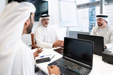 Dubai 'deki ofiste geleneksel emirati kıyafetleri giyen bir grup orta doğulu iş adamı BAE' de çalışıyor ve beyin fırtınası yapıyor.