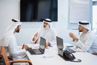Dubai 'deki ofiste geleneksel emirati kıyafetleri giyen bir grup orta doğulu iş adamı BAE' de çalışıyor ve beyin fırtınası yapıyor.