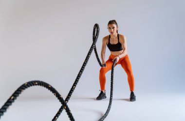 Spor aletlerini kullanarak spor salonunda antrenman yapan genç bir bayan sporcu. Formda kadın vücut çalışıyor. Zindelik, sağlık ve spor hazırlığı kavramları.