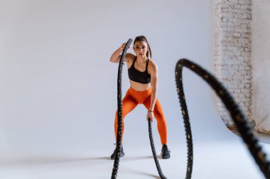 Spor aletlerini kullanarak spor salonunda antrenman yapan genç bir bayan sporcu. Formda kadın vücut çalışıyor. Zindelik, sağlık ve spor hazırlığı kavramları.