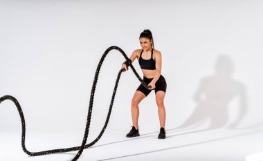 Spor aletlerini kullanarak spor salonunda antrenman yapan genç bir bayan sporcu. Formda kadın vücut çalışıyor. Zindelik, sağlık ve spor hazırlığı kavramları.