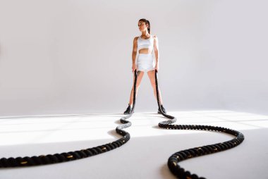 Spor aletlerini kullanarak spor salonunda antrenman yapan genç bir bayan sporcu. Formda kadın vücut çalışıyor. Zindelik, sağlık ve spor hazırlığı kavramları.