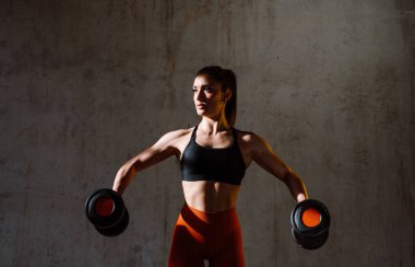 Spor aletlerini kullanarak spor salonunda antrenman yapan genç bir bayan sporcu. Formda kadın vücut çalışıyor. Zindelik, sağlık ve spor hazırlığı kavramları.