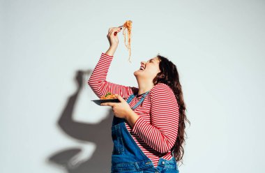 Artı stüdyoda poz veren ve eğlenen boy kadın modeller. Mutlu model domatesli İtalyan spagettisi yiyor.