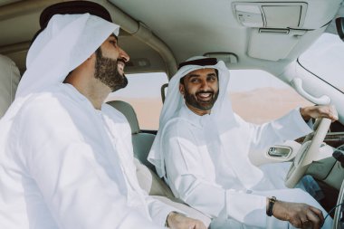 Geleneksel emirati Arap kandurası giyen iki orta doğulu çölde 4x4 'lük bir araba kullanıyor - Arap Müslüman arkadaşlar Dubai' de kum tepelerinde bir gezintiye çıkıyorlar.