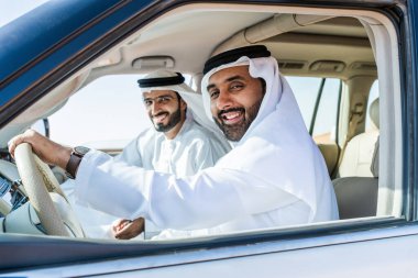 Geleneksel emirati Arap kandurası giyen iki orta doğulu çölde 4x4 'lük bir araba kullanıyor - Arap Müslüman arkadaşlar Dubai' de kum tepelerinde bir gezintiye çıkıyorlar.