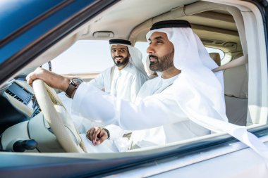 Geleneksel emirati Arap kandurası giyen iki orta doğulu çölde 4x4 'lük bir araba kullanıyor - Arap Müslüman arkadaşlar Dubai' de kum tepelerinde bir gezintiye çıkıyorlar.