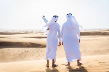 Çölde geleneksel emirati Arap kandurası giyen iki ortadoğulu Müslüman arkadaş Dubai 'deki kum tepelerinde buluşuyor.
